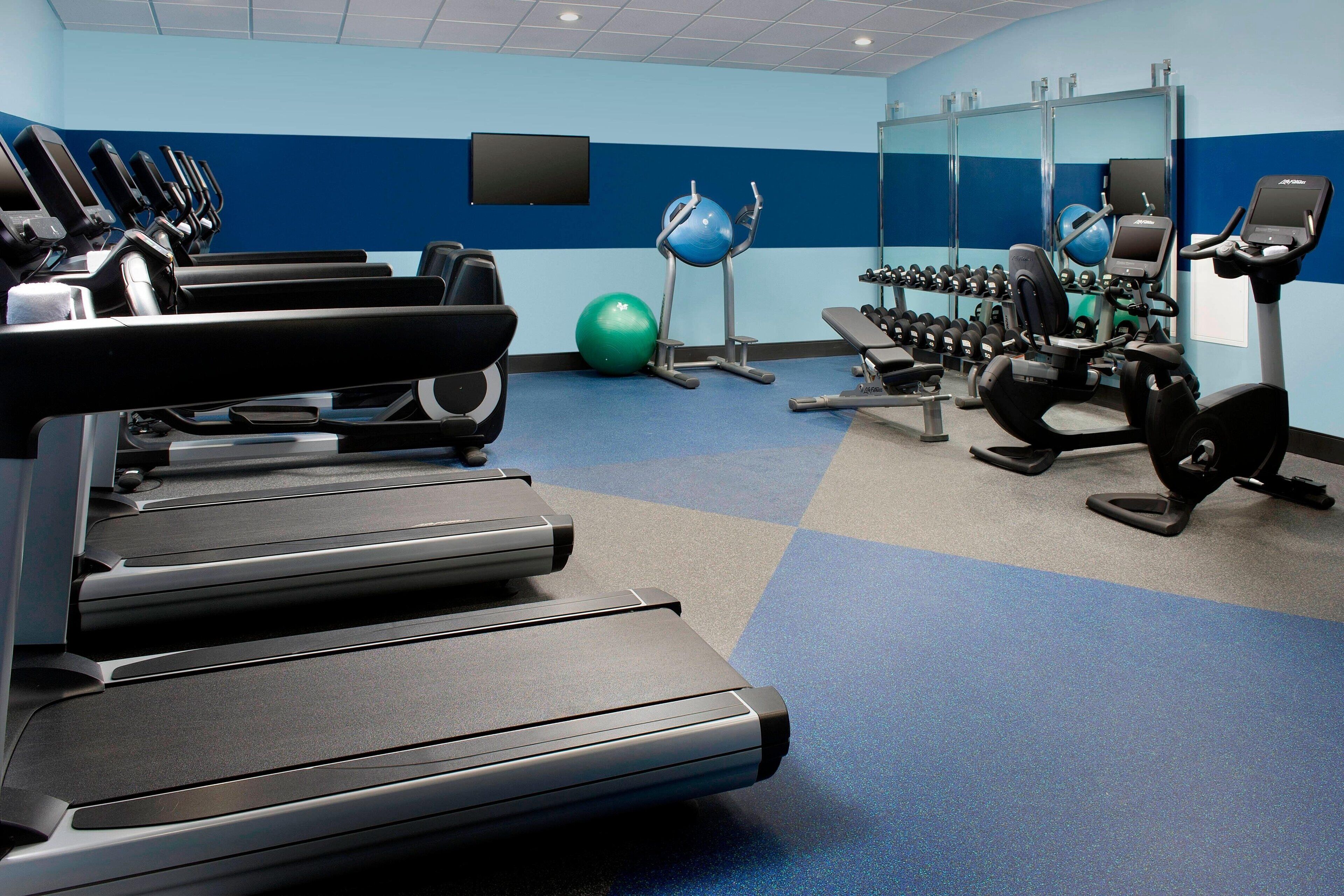 Un gimnasio con cintas de correr, pelotas de ejercicio y mancuernas.