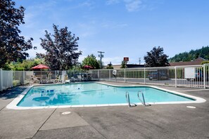 Piscina retangular ao ar livre com cerca branca, cercada por árvores e céu claro.