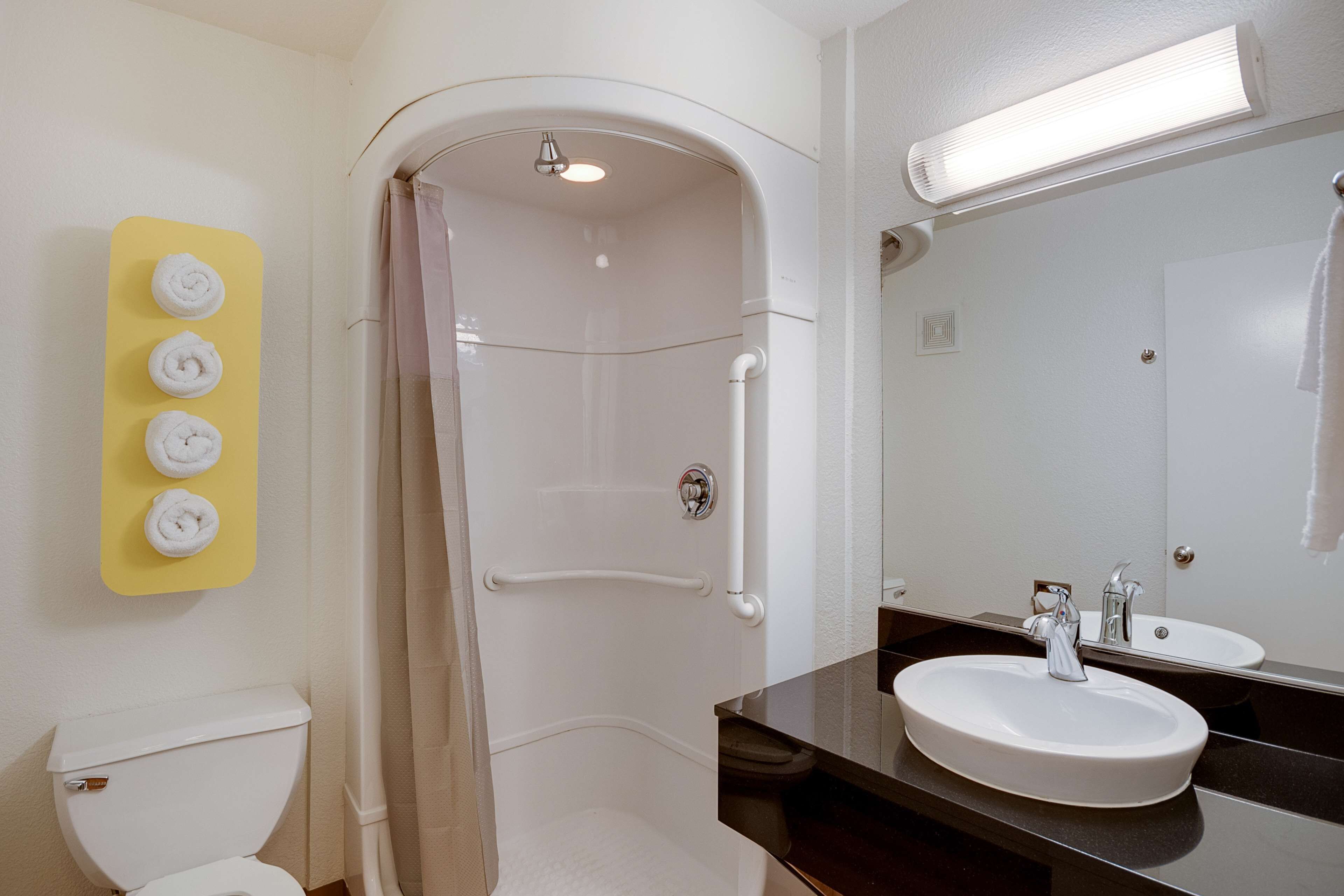 Un baño con inodoro blanco, ducha con puerta de cristal, toallero amarillo con cuatro toallas y un espejo grande sobre un lavamanos.