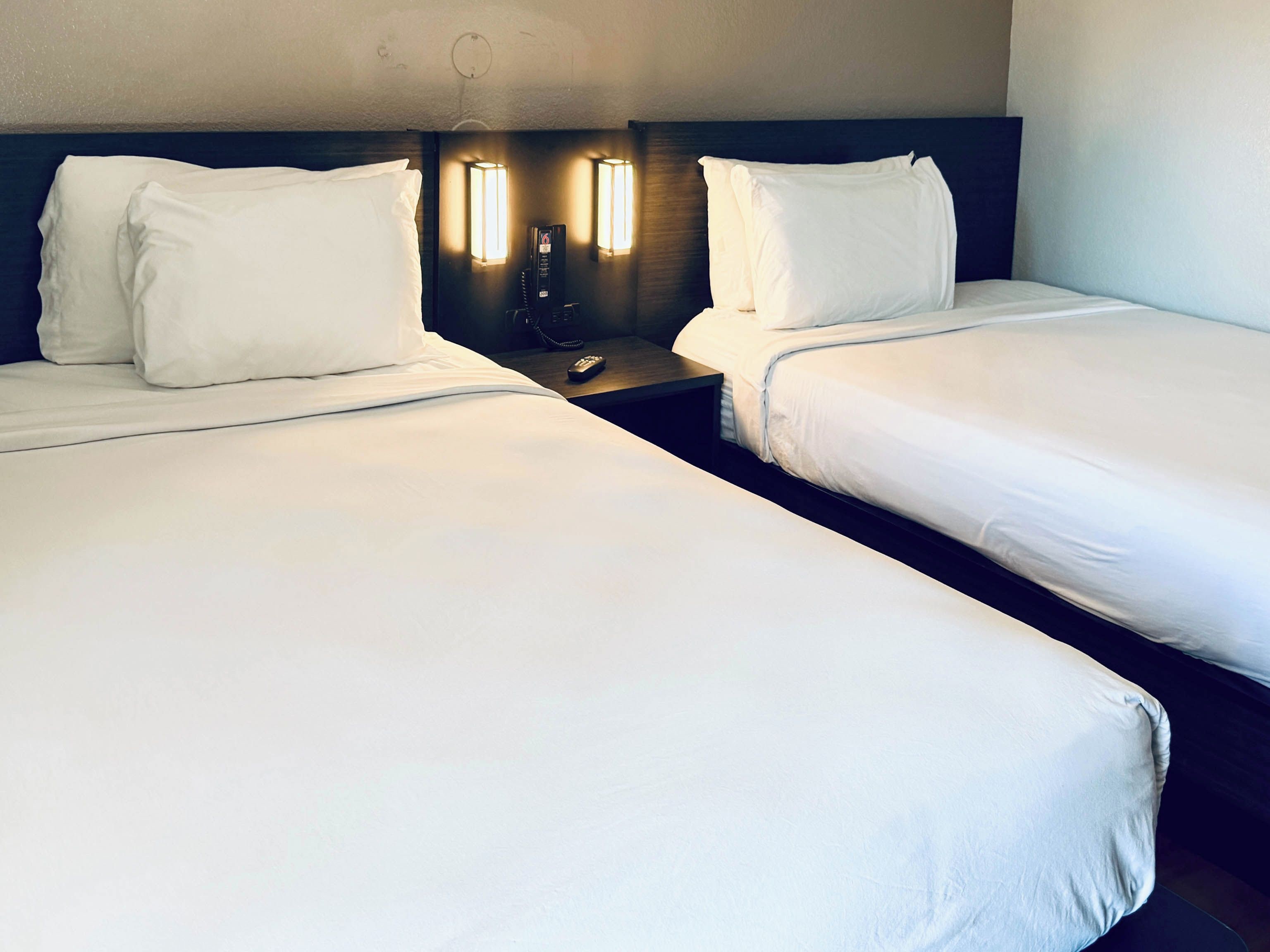 A hotel room with two single beds, a bedside table with a phone, and wall-mounted lights.
