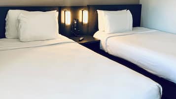 A hotel room with two single beds, a bedside table with a phone, and wall-mounted lights.