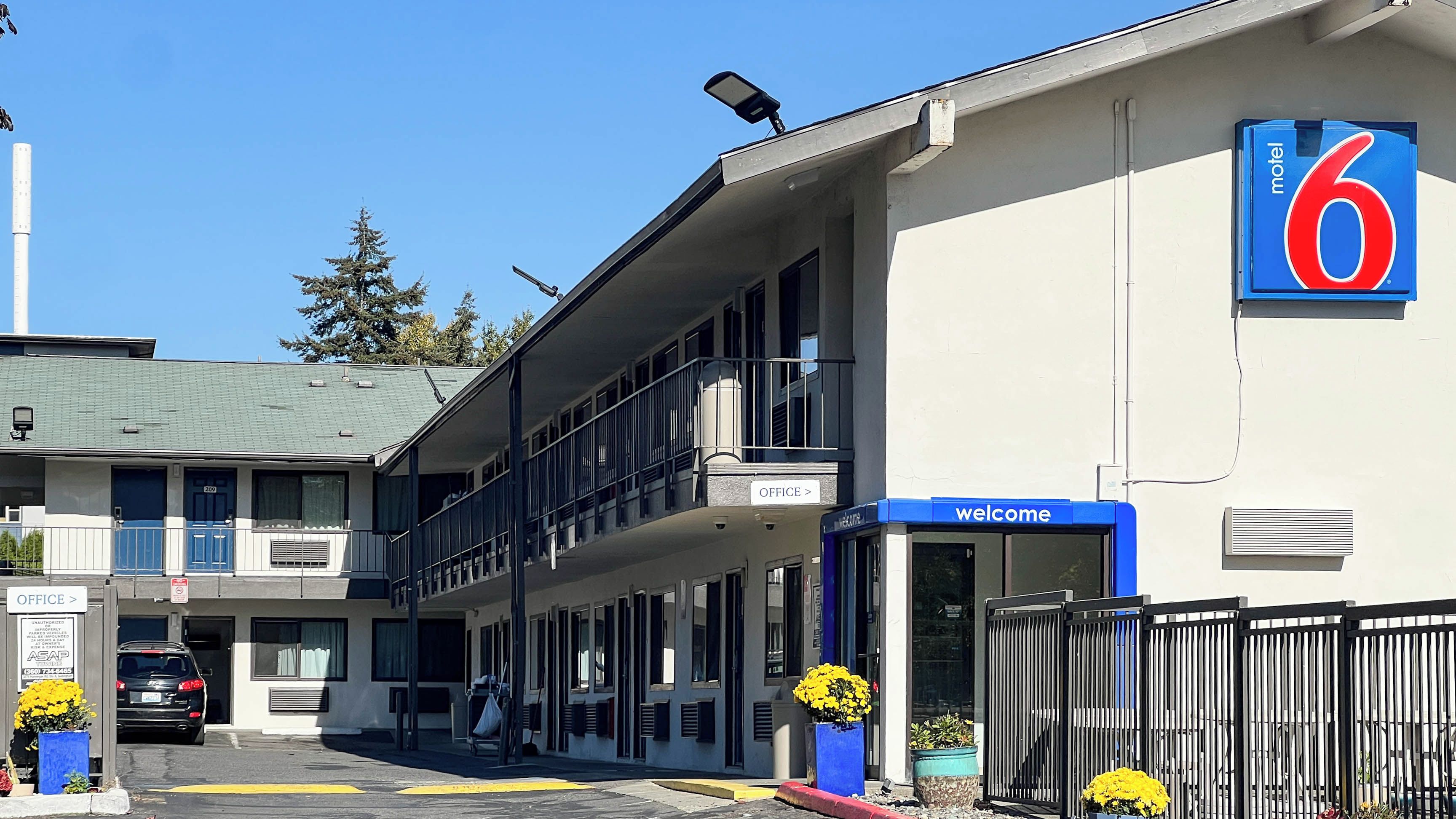Um motel com placa de '6', entrada de escritório e placa de boas-vindas.