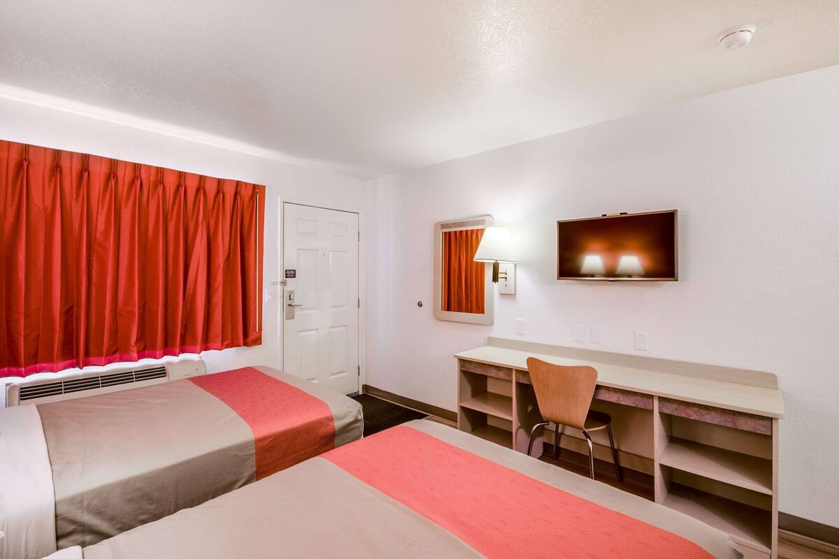 Habitación de hotel con dos camas, un escritorio, una silla, un televisor y una ventana con cortinas.