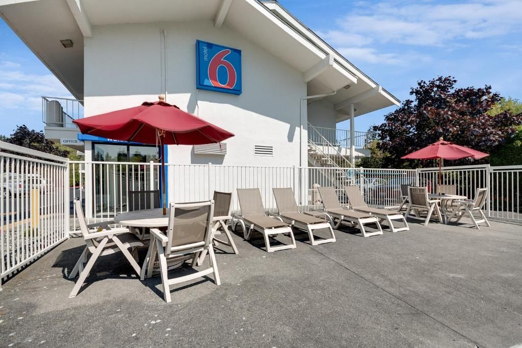 A motel with a number '6' sign, outdoor seating with tables and chairs, and red umbrellas.