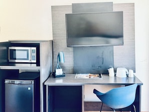 Quarto de hotel compacto com cozinha compacta, televisão de tela plana, uma cadeira azul e uma pequena geladeira.