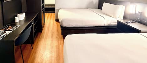 A hotel room with two beds, a desk, a television, and a small window.