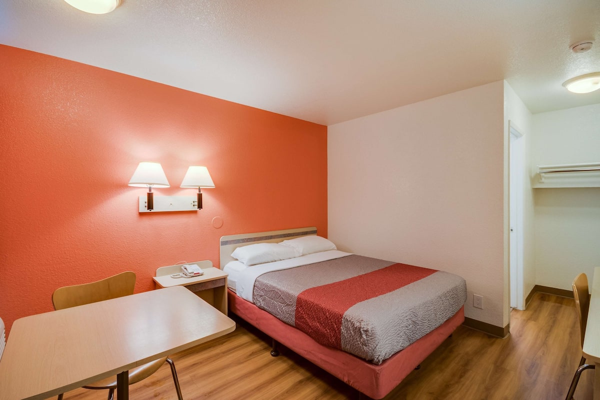 Una habitación de hotel con una cama, un escritorio, una silla y una lámpara de pared.