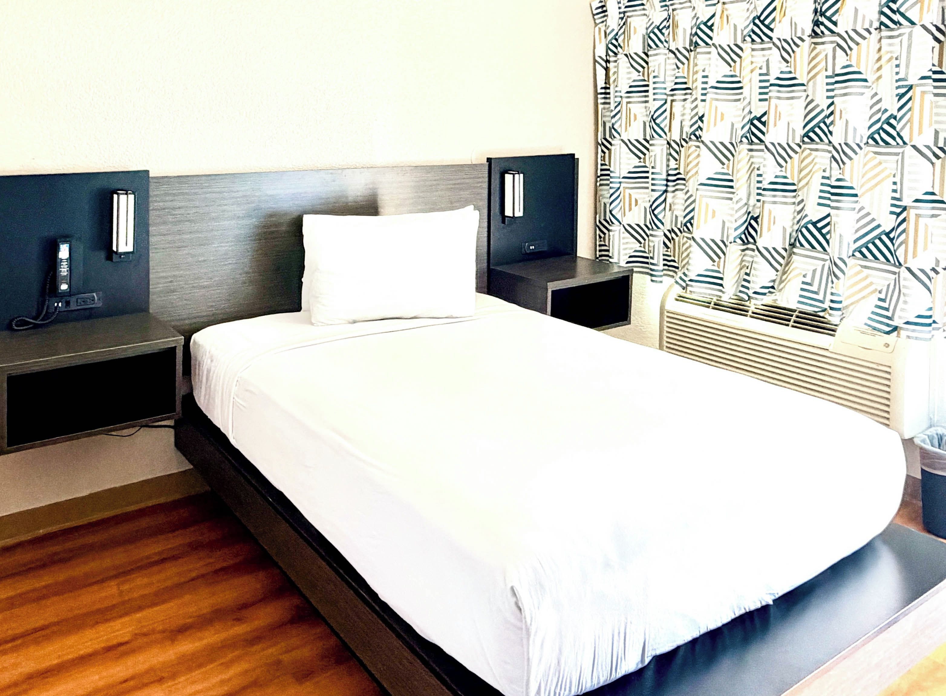 A hotel room with a large bed, bedside tables, a phone, and a patterned curtain.