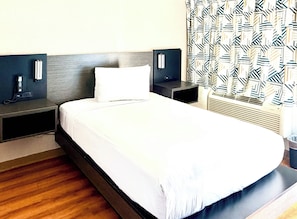 Quarto de hotel com uma cama grande, mesas de cabeceira, um telefone e cortina estampada.