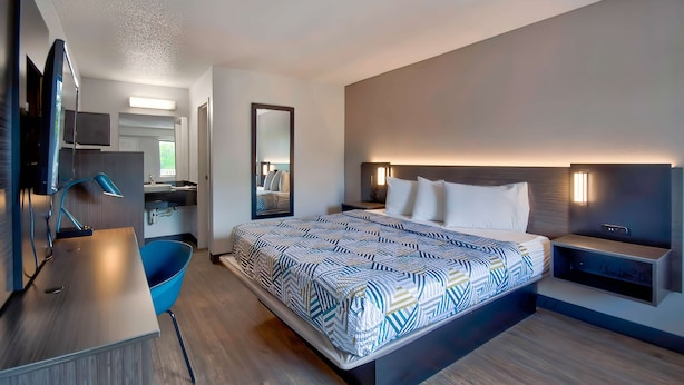 A modern hotel room with a large bed, bedside tables, a desk, and a chair. - Motel 6 Warren, MI - Detroit East (Warren)