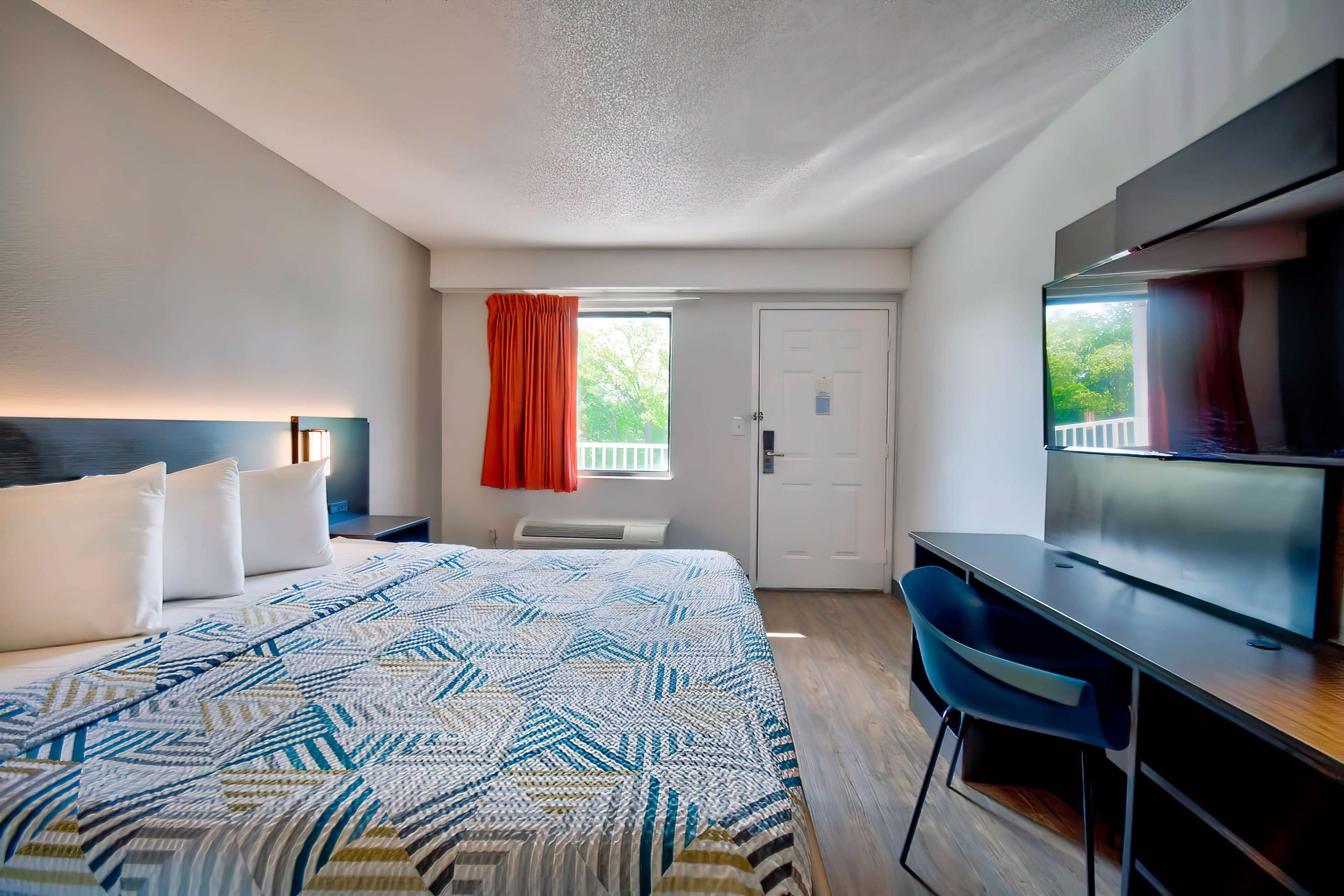 A hotel room with a bed, a desk, a chair, a TV, and a window with curtains.