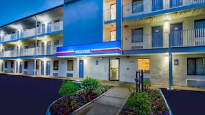 A motel with a blue exterior and a 'WELCOME' sign. It has multiple floors with balconies and a parking area with flower beds. - Motel 6 Warren, MI - Detroit East (Warren)