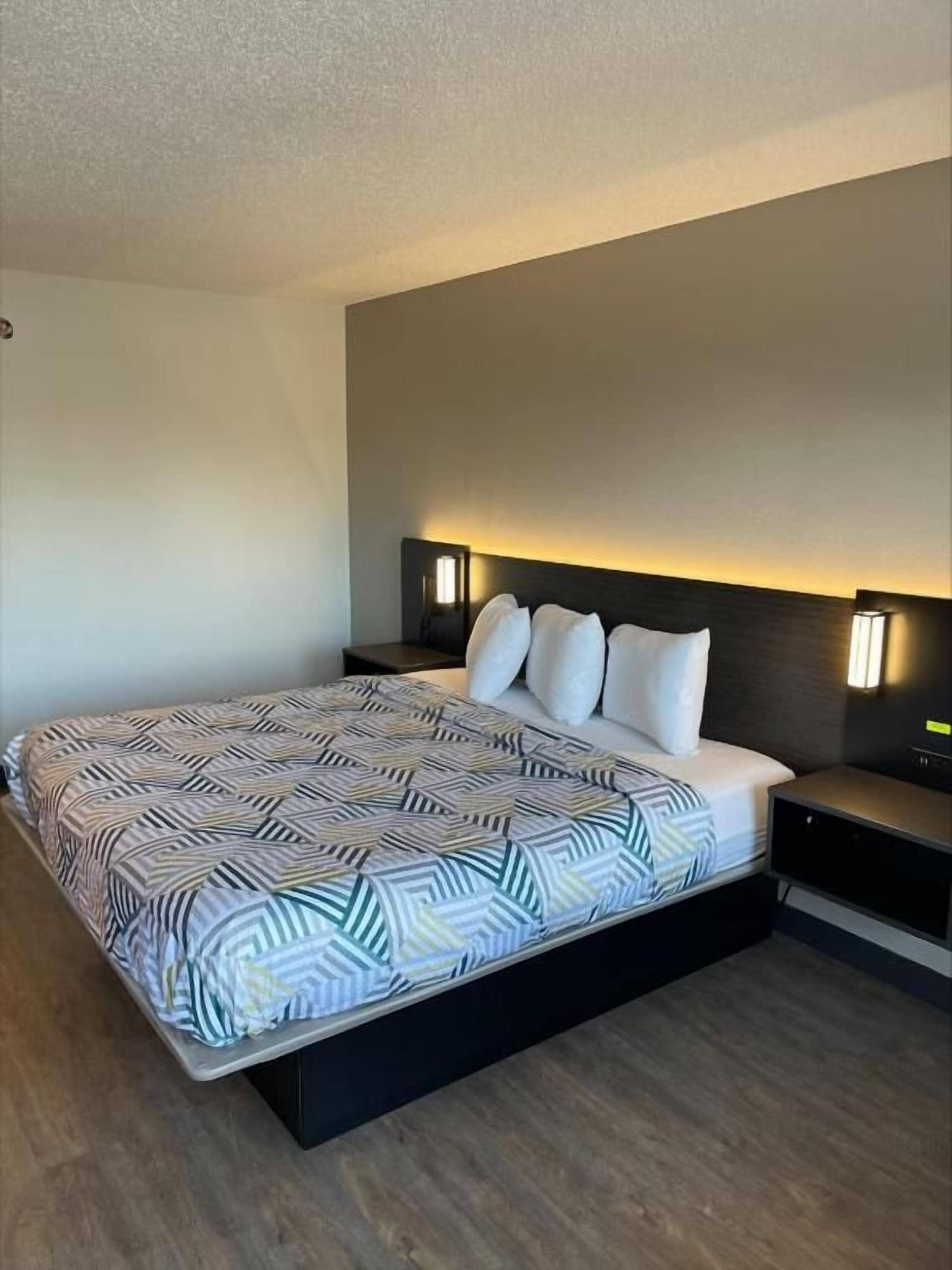 A modern hotel room with a large bed, bedside lamps, and a dark headboard.