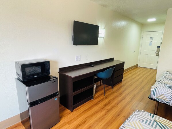 A compact room with a kitchenette, a desk, a chair, a bed, and a television. - Motel 6 Duncanville, TX - Dallas (Duncanville)