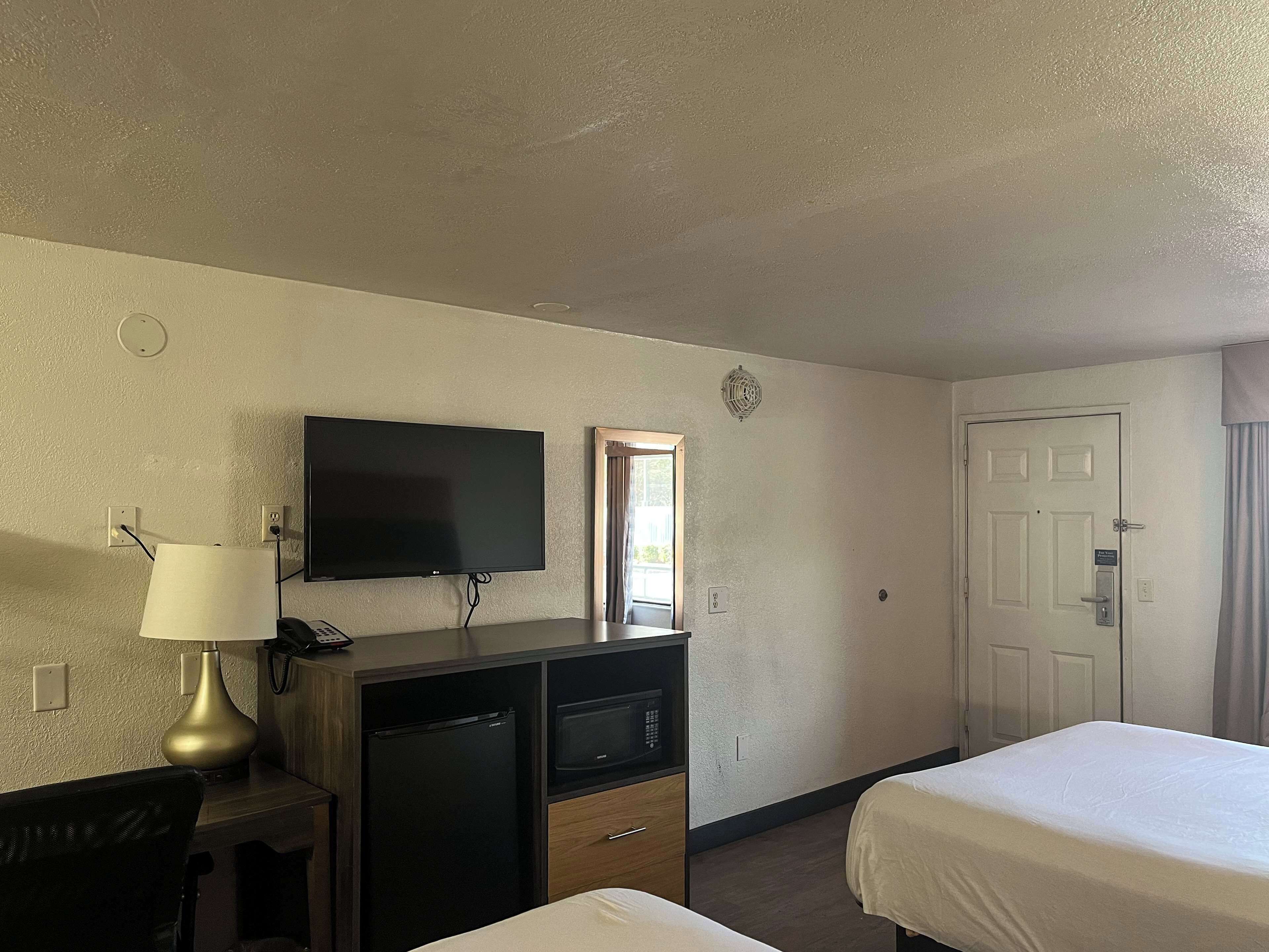 A hotel room with a television, desk, refrigerator, and two beds.