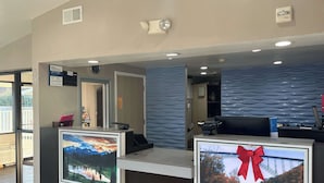 A reception desk with a mounted TV, a fire alarm, and a clock on the wall. - Motel 6 Cross Lanes, WV - Goff Mountain Rd (Cross Lanes)
