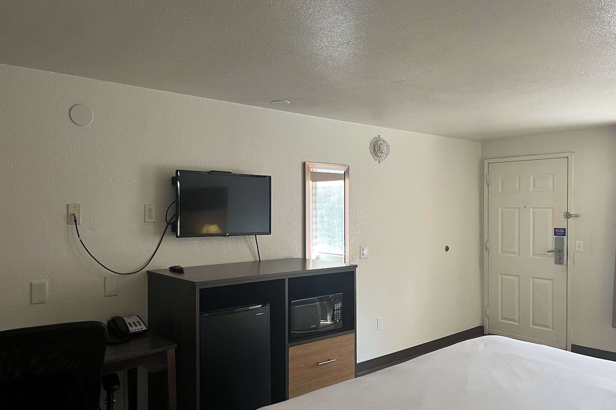A hotel room with a bed, a desk with a telephone, a television mounted on the wall, a microwave, and a door with a lock.