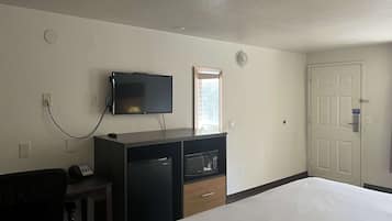 A hotel room with a bed, a desk with a telephone, a television mounted on the wall, a microwave, and a door with a lock.
