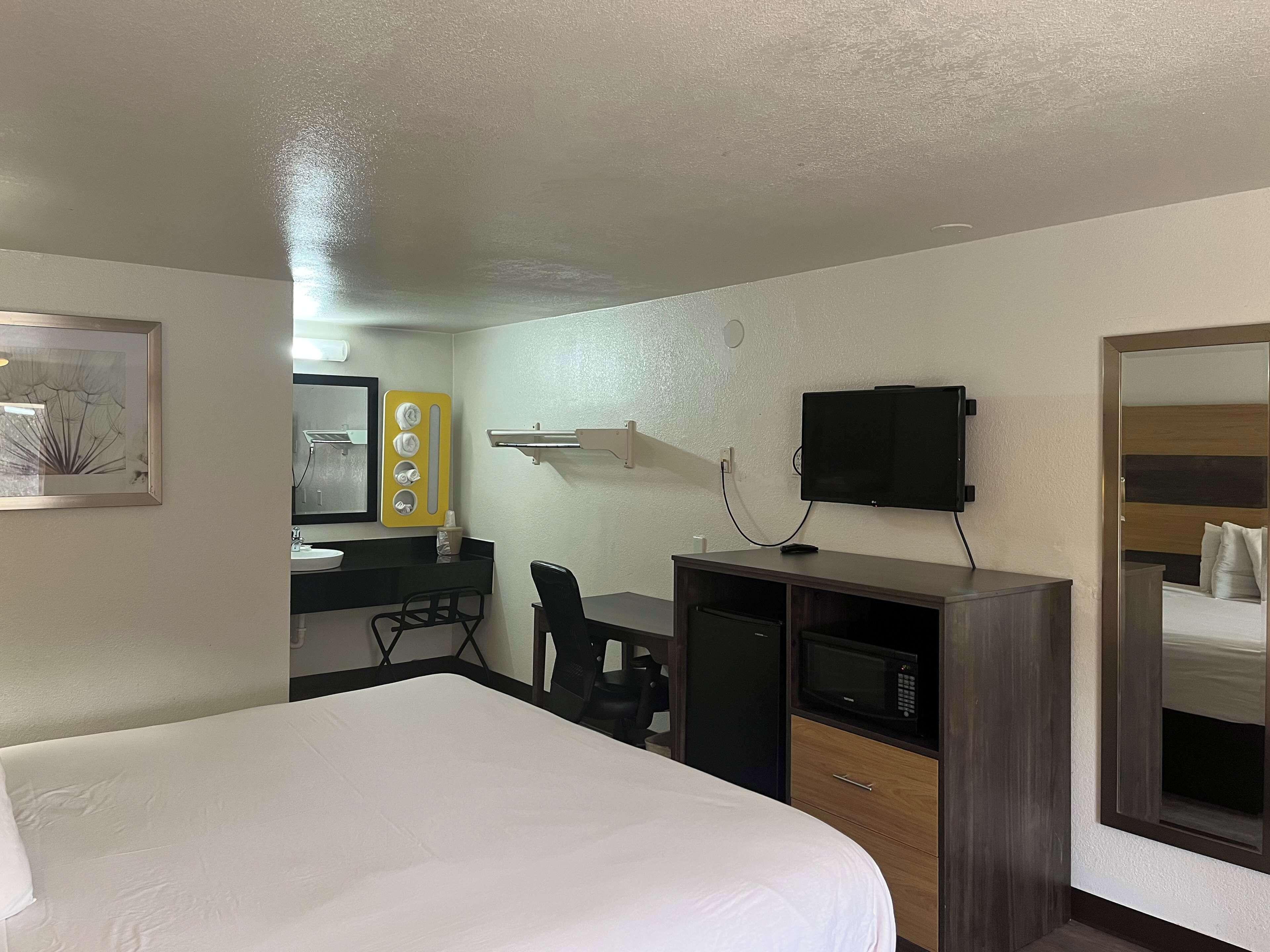 A hotel room with a bed, a desk with a computer, a TV, and a microwave.