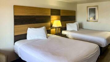 A hotel room with two beds, a nightstand with a lamp, and a painting on the wall.