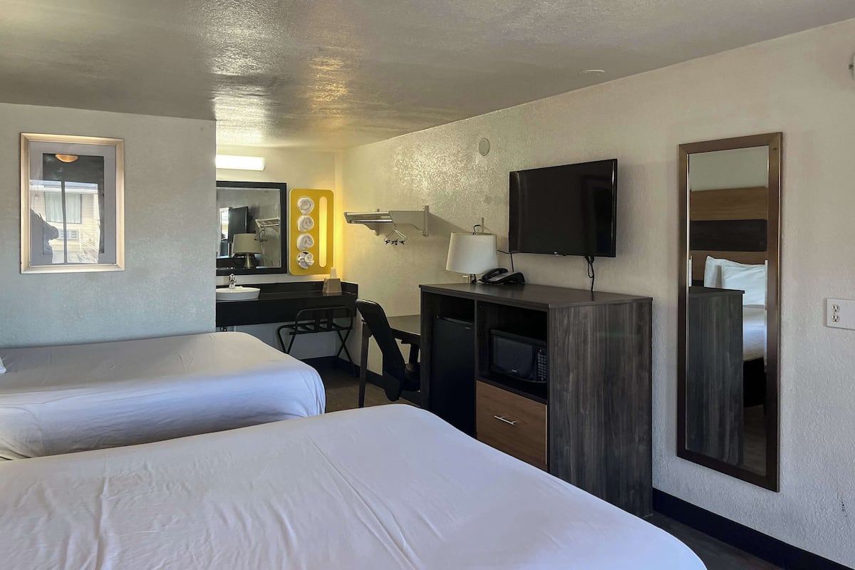 A hotel room with two beds, a desk with a computer, a TV, and a mirror.