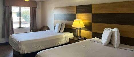 Ein Hotelzimmer mit zwei Betten, einem Schreibtisch, einem Stuhl, einer Lampe und einem Fenster mit Vorhängen.