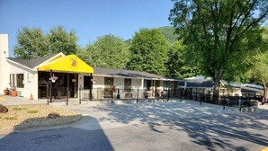 A motel with a yellow front entrance, a covered parking area, and a row of rooms with a mountain backdrop.