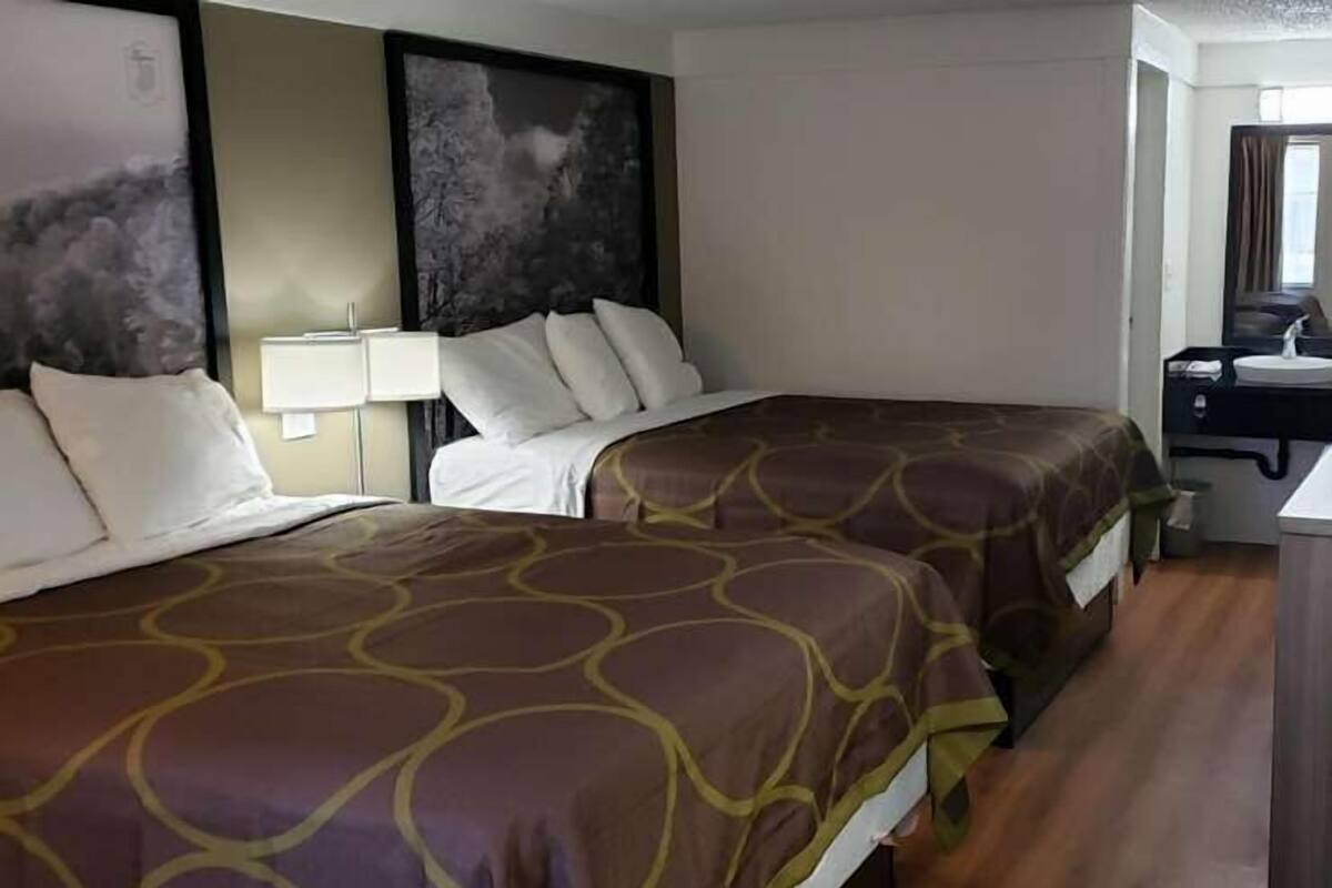A hotel room with two beds, a desk with a sink, and artwork on the walls.