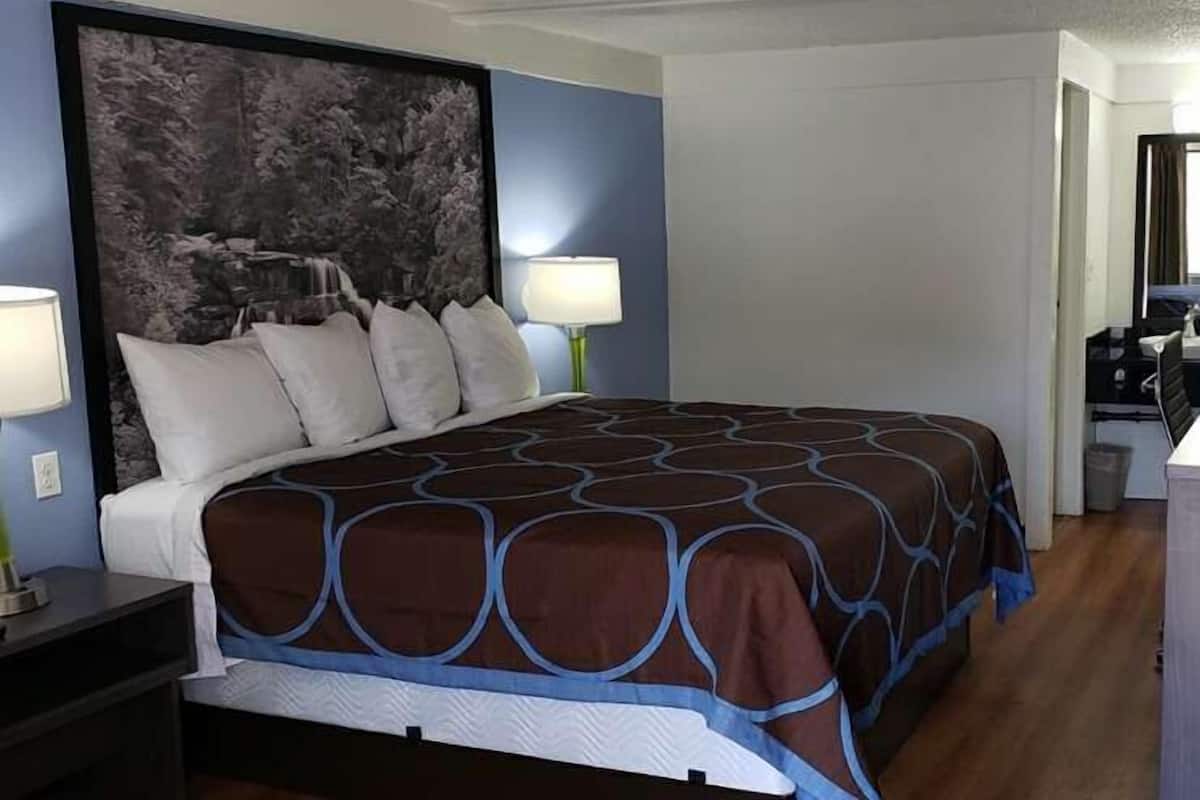 A hotel room with a large bed, two bedside lamps, a nightstand, and a painting on the wall.