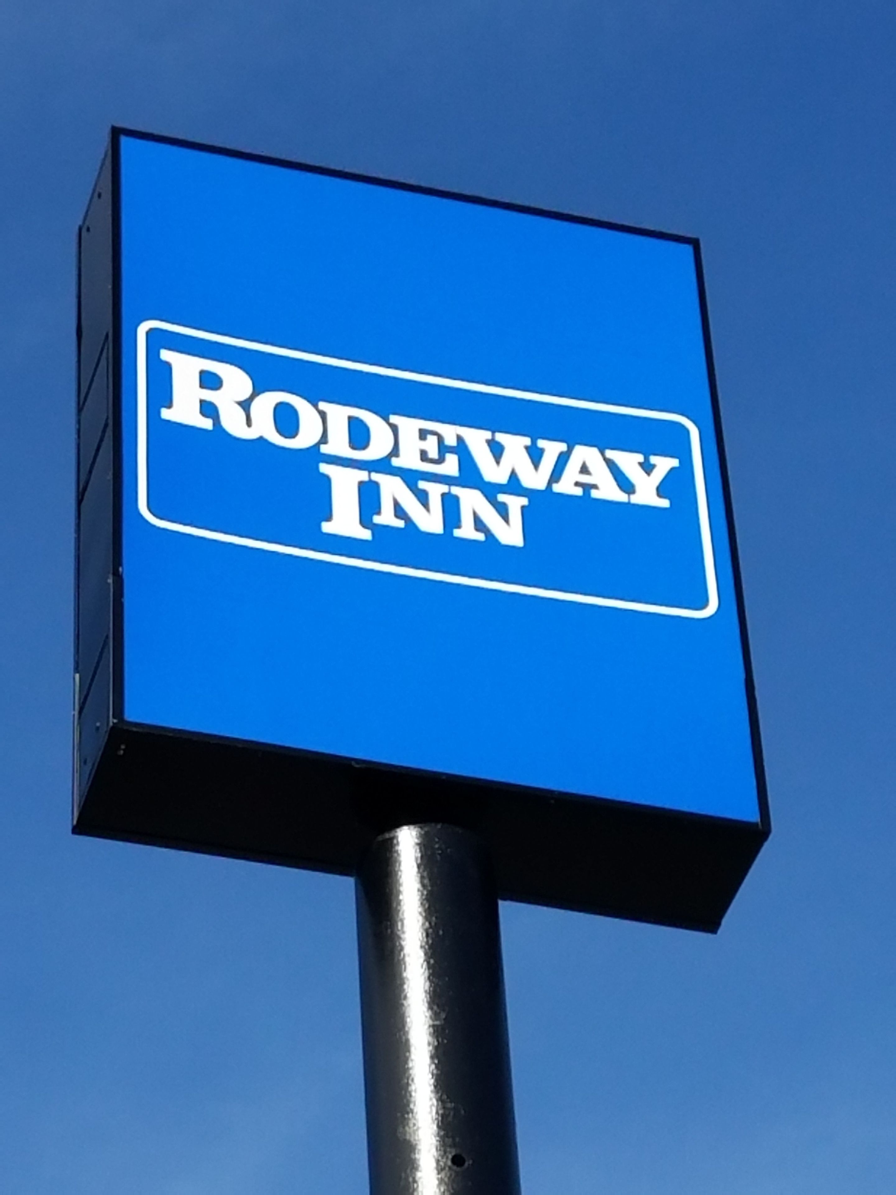 Un letrero azul con el texto 'Rodeway Inn' sobre un cielo despejado.