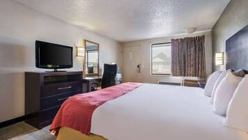 A hotel room with a large bed, a desk with a chair, a television, a window with curtains, and a door.