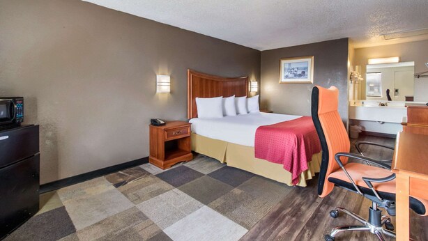 A hotel room with a bed, a desk, a chair, a microwave, and a small cabinet. - Rodeway Inn Near Hall of Fame (North Canton)
