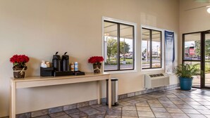 A reception area with a wooden desk, two red flower arrangements, a trash can, and a potted plant. - Rodeway Inn Near Hall of Fame (North Canton)
