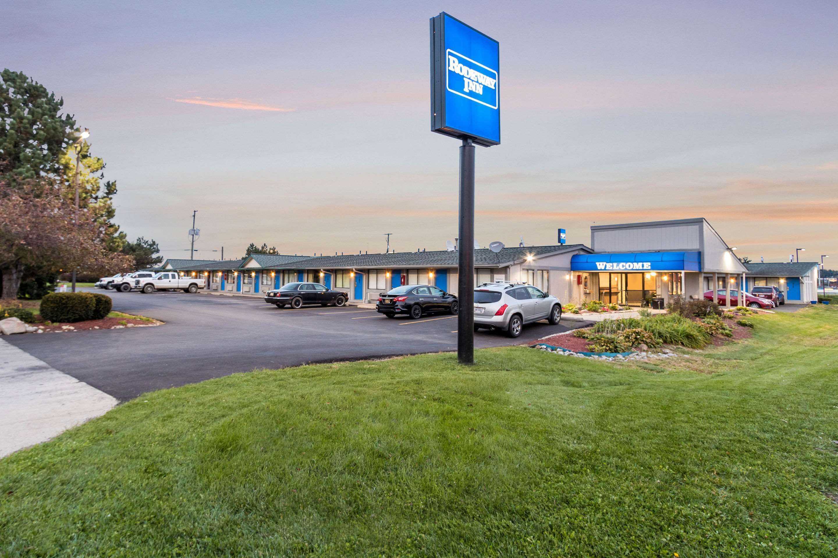 A motel with a blue sign, a parking lot, and a building with a 'Welcome' sign.