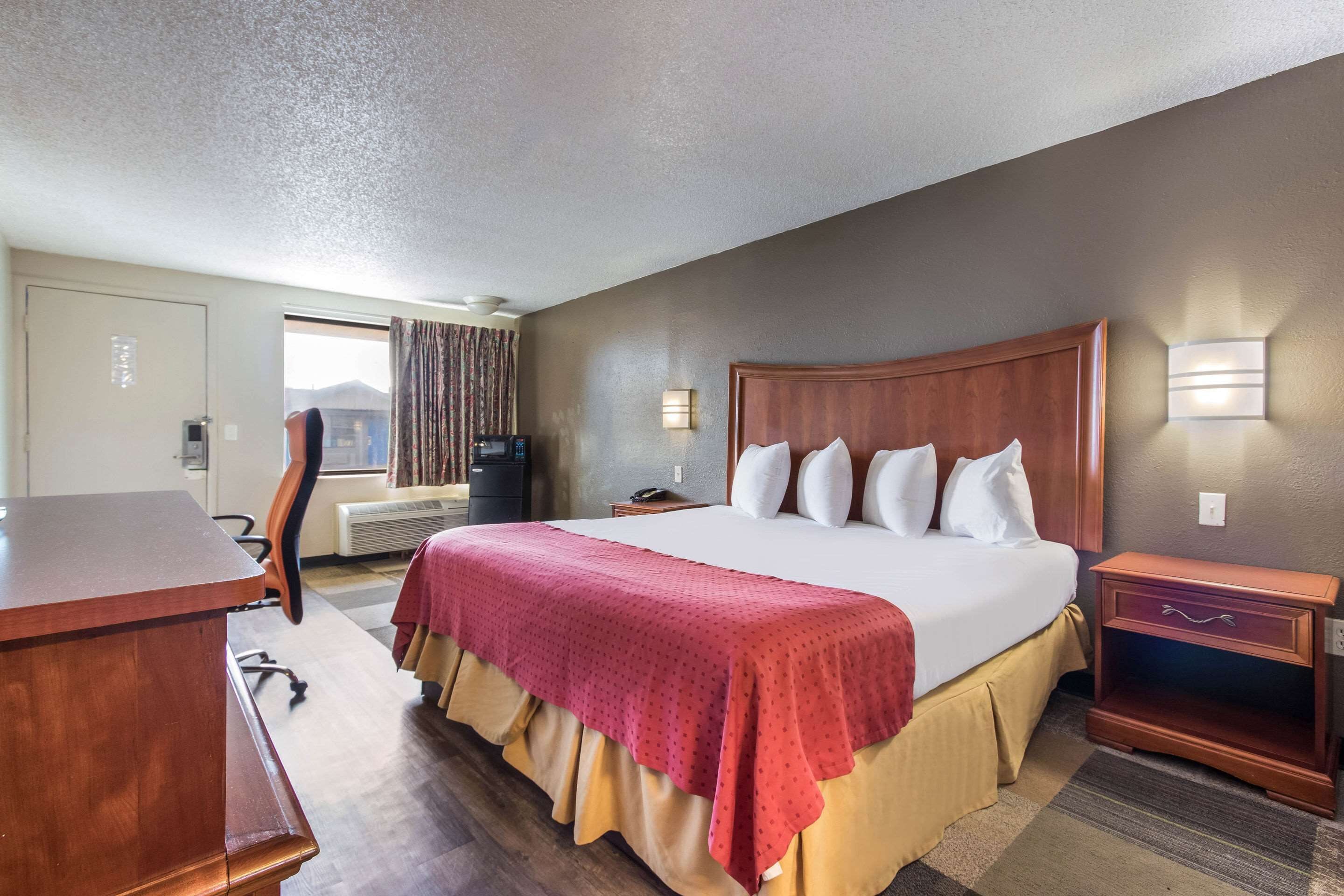 Quarto de hotel com uma cama grande, uma escrivaninha, uma cadeira, uma televisão e uma janela com cortinas.