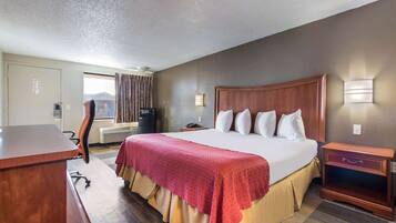 Quarto de hotel com uma cama grande, uma escrivaninha, uma cadeira, uma televisão e uma janela com cortinas.