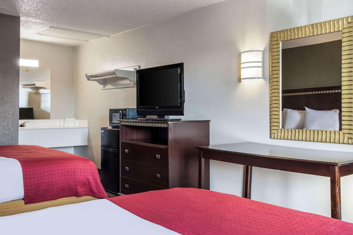 Habitación de hotel con dos camas, televisión, cómoda, espejo y escritorio.
