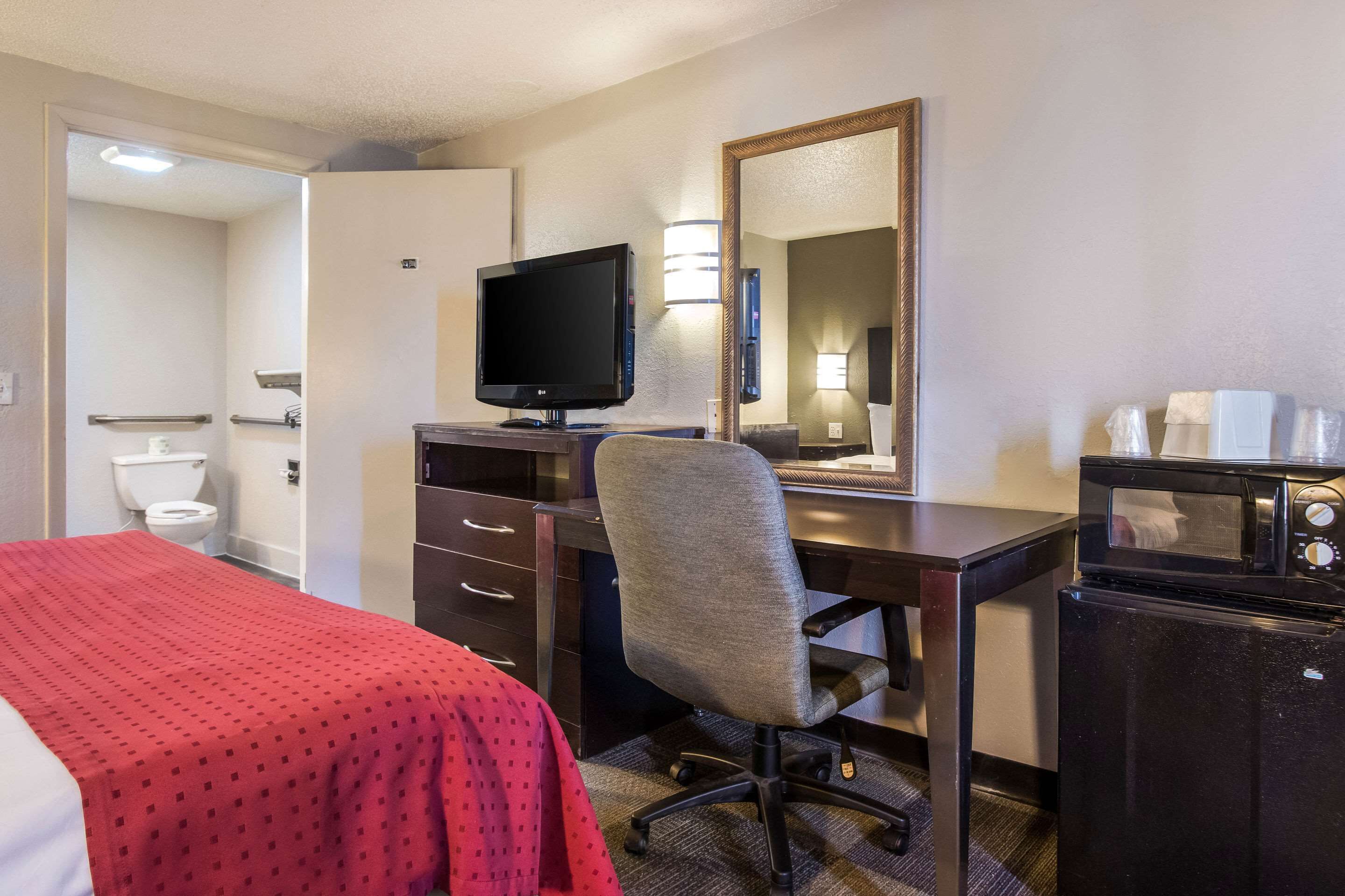 A hotel room with a bed, a desk with a computer and a TV, a microwave, and a refrigerator.
