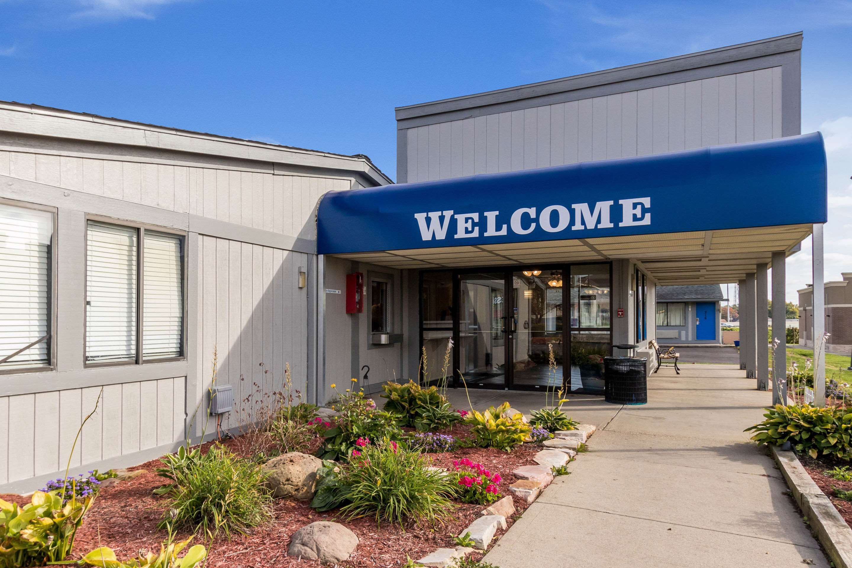 A building with a 'WELCOME' sign, a covered entrance, and a landscaped garden area.