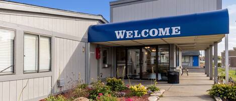 A building with a 'WELCOME' sign, a covered entrance, and a landscaped garden area.
