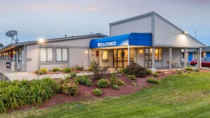 A modern building with a "WELCOME" sign, a covered entrance, and a landscaped garden area. - Rodeway Inn Near Hall of Fame (North Canton)