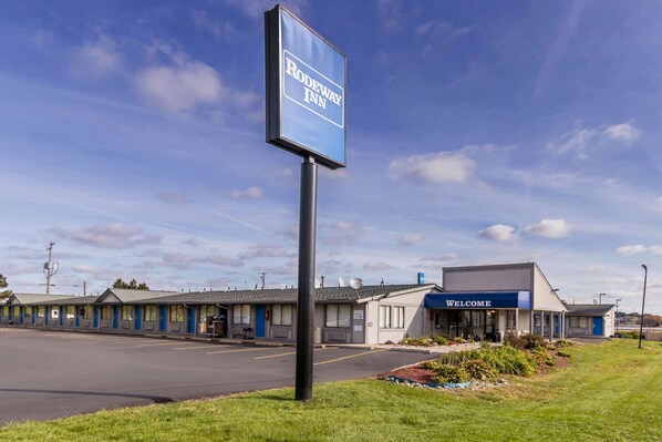 A motel with a signboard for Rodeway Inn, featuring a simple building layout with a 'Welcome' sign, a parking lot, and a grassy area.