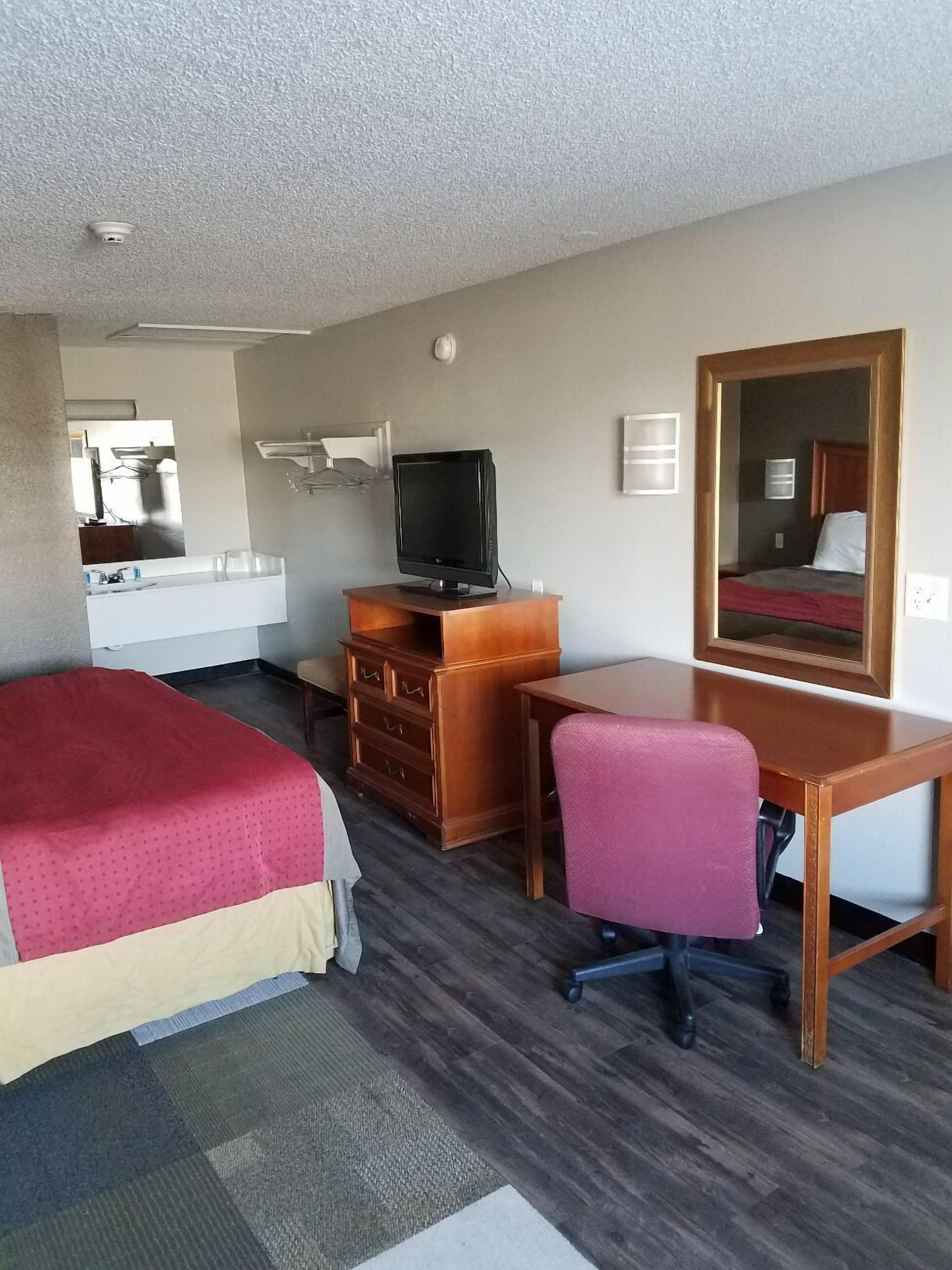 Ein Hotelzimmer mit zwei Betten, einem Schreibtisch mit Stuhl, einem Fernseher, einem Schminktisch und einem Spiegel. Im Hintergrund ist ein Badezimmer zu sehen.