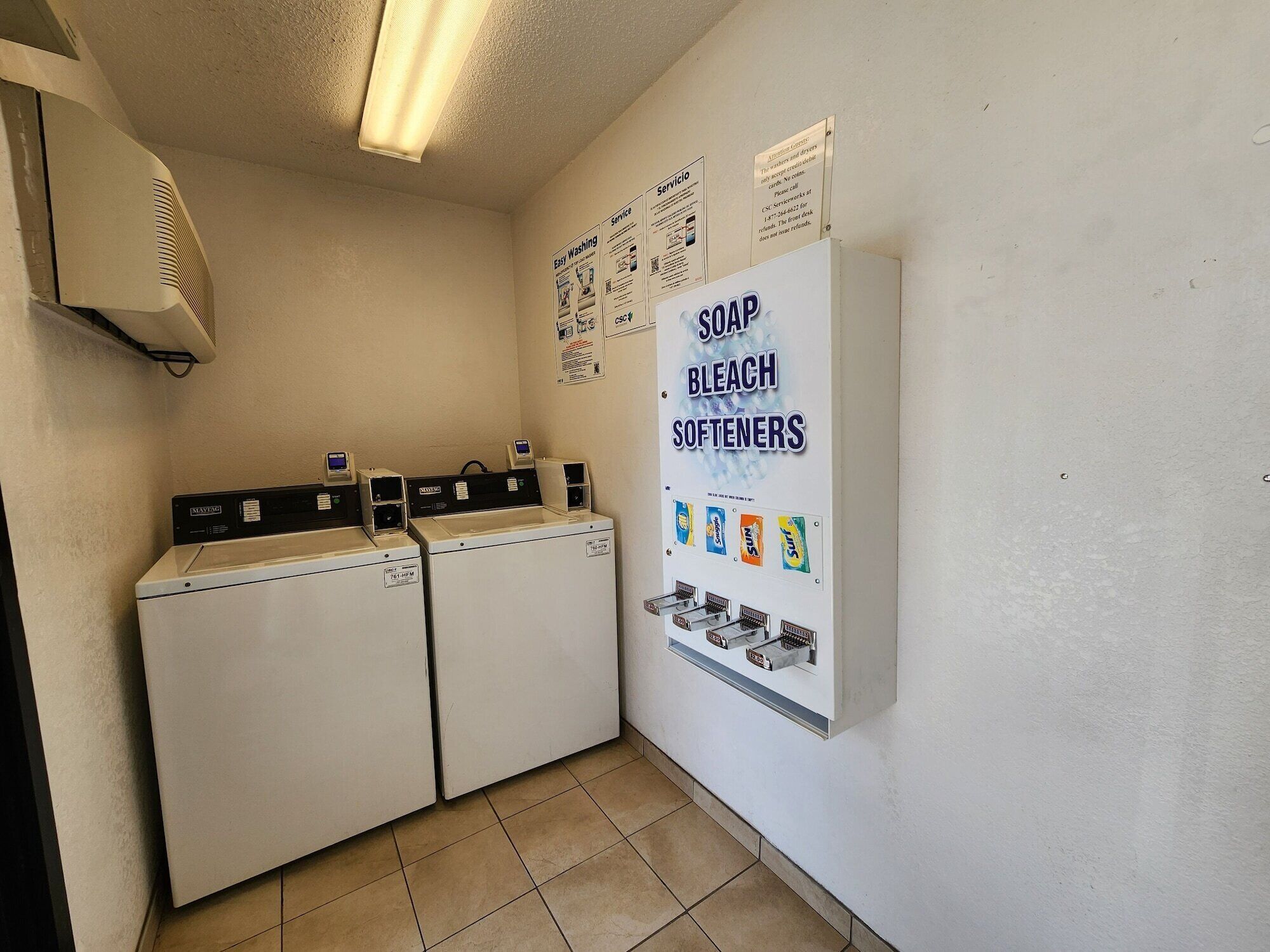 Un espace buanderie comprenant deux lave-linge à chargement frontal, un sèche-linge et un distributeur mural pour le savon, l’eau de Javel et l’adoucissant.