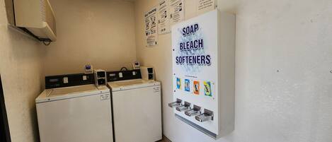 Un espace buanderie comprenant deux lave-linge à chargement frontal, un sèche-linge et un distributeur mural pour le savon, l’eau de Javel et l’adoucissant.