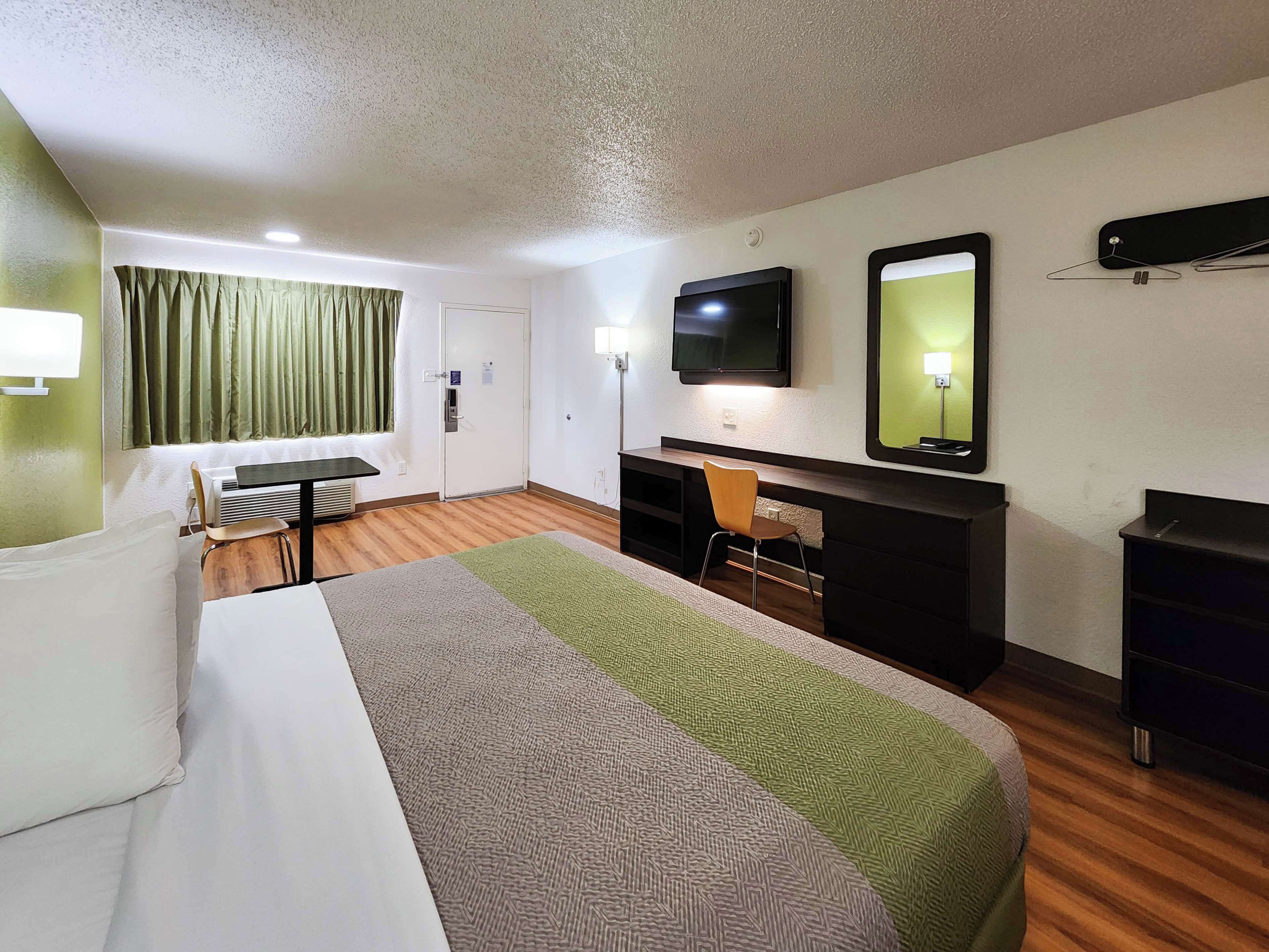 A hotel room with a bed, a desk, a chair, a TV, a mirror, and a wardrobe.