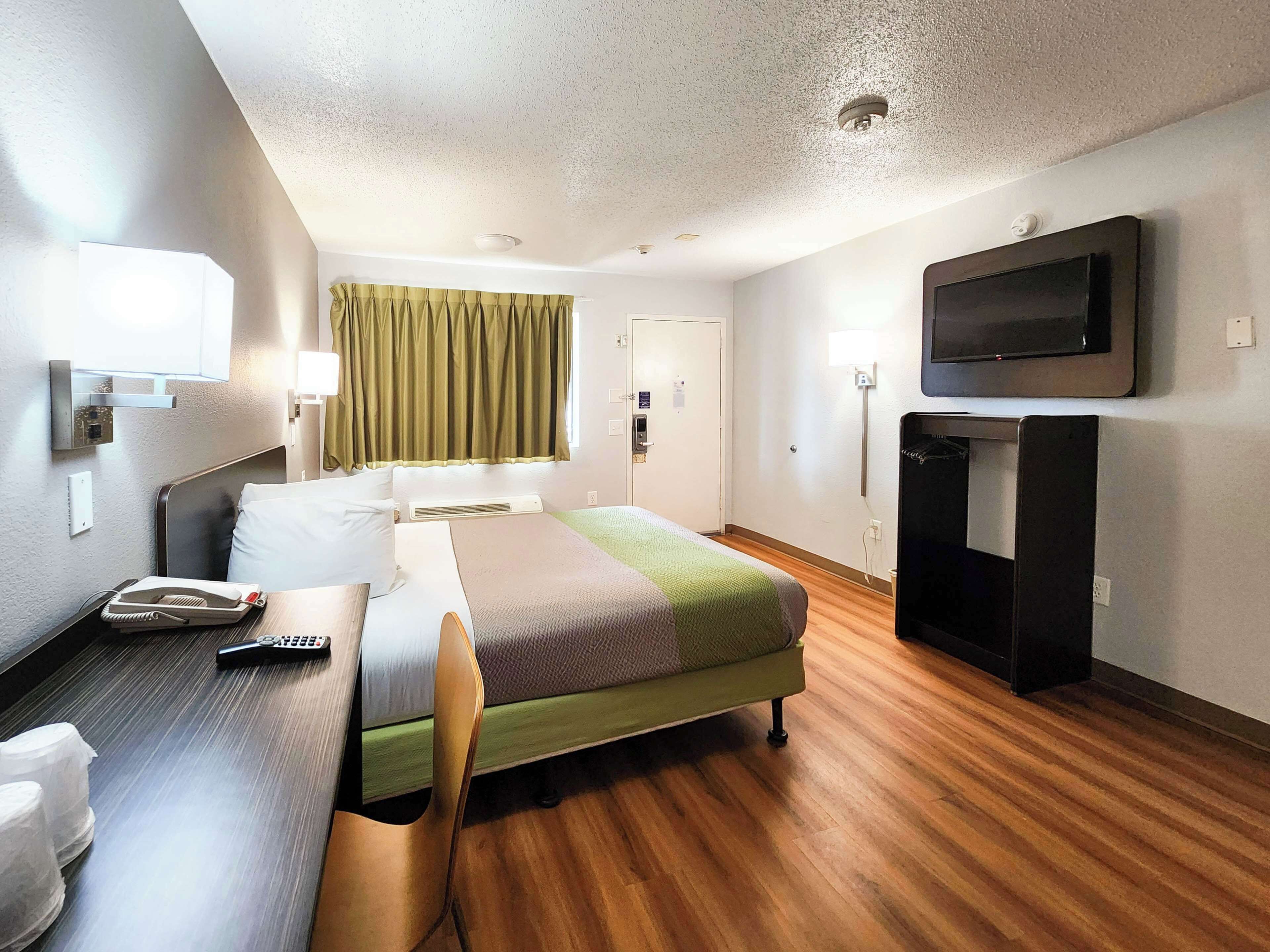 A hotel room with a bed, a desk, a chair, a television, and a window with curtains.