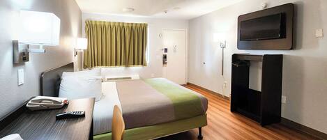 A hotel room with a bed, a desk, a chair, a television, and a window with curtains.