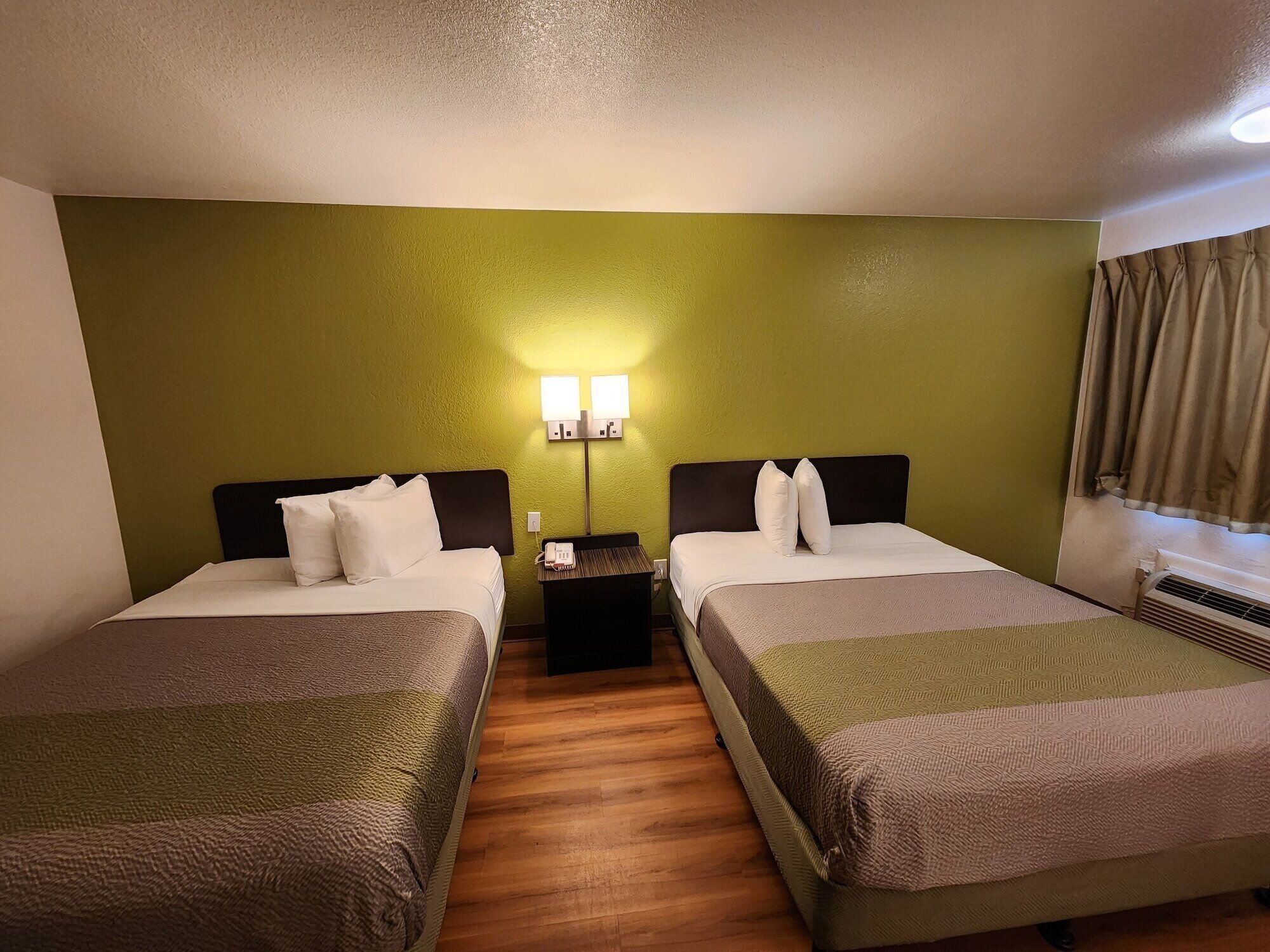 A hotel room with two beds, a nightstand, a lamp, and a window with curtains.