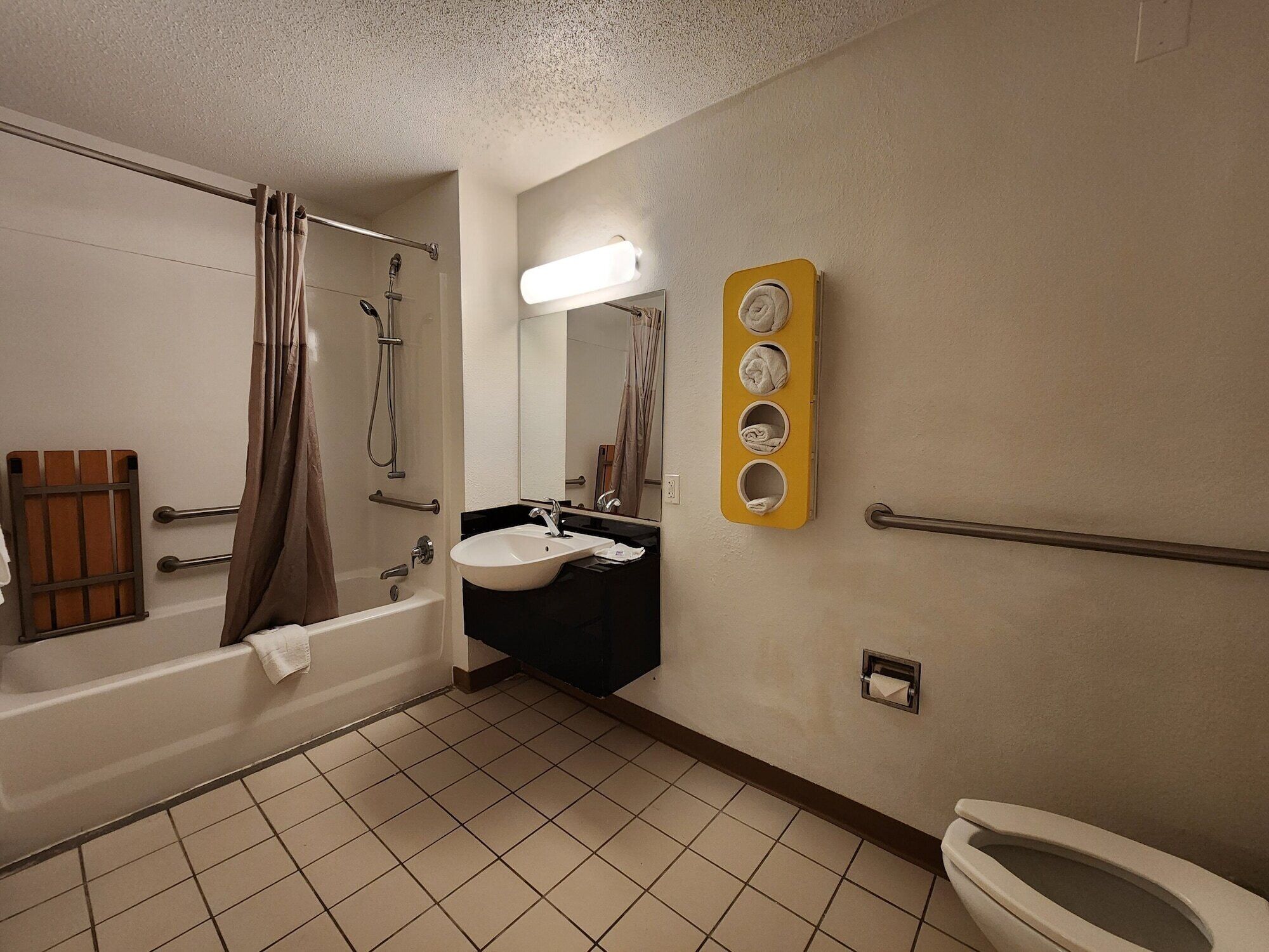 Een badkamer met een bad, wastafel en toilet. Er is een handdoekhouder en een spiegel.